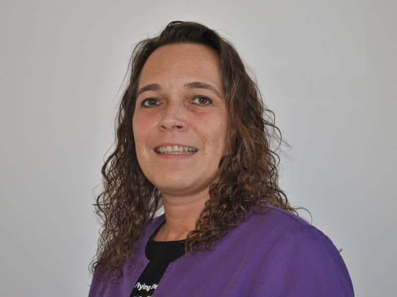 Portraitfoto von Sina Pabst, Mitarbeiterin der Hausarztpraxis Neumünden in Hann. Münden. Sie trägt eine violette Kasack und lächelt freundlich in die Kamera. Frau Pabst ist verantwortlich für den Empfang sowie die organisatorische Betreuung von Medizinstudierenden in der Lehrpraxis.